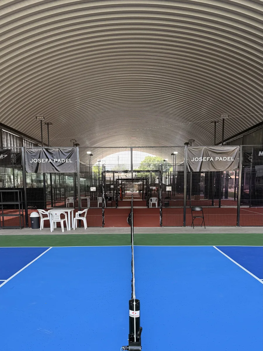 Cancha de pickleball azul de frente, con las canchas de pádel techadas al fondo