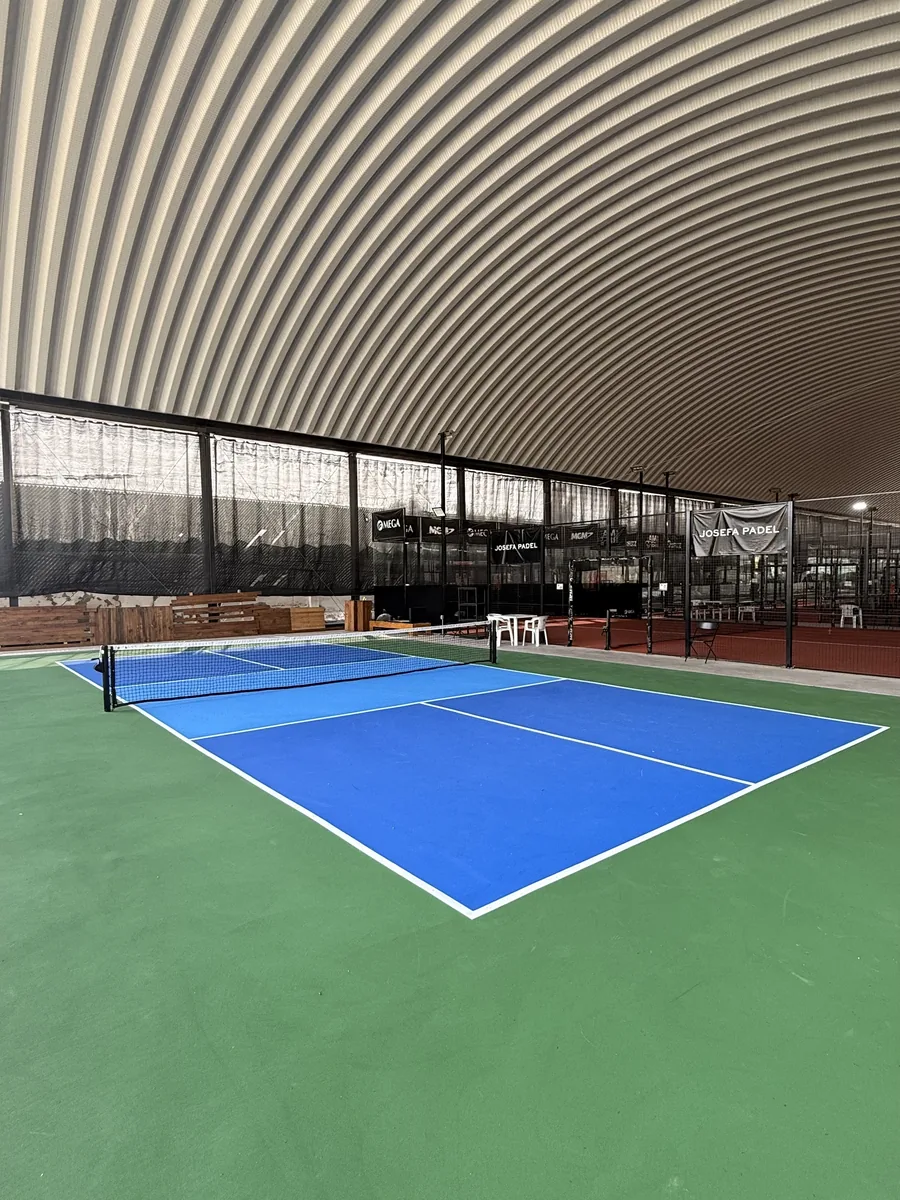 Cancha de pickleball completa, con el piso verde alrededor y el techo de arco del club